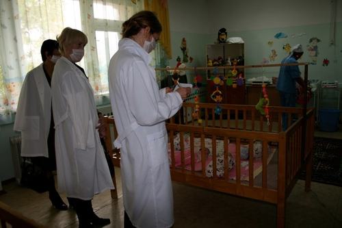 Photo of two people in lab coats taking notes while looking at a baby crib