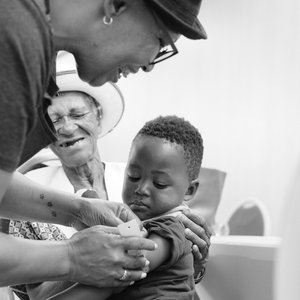 A black and white photo of a woman measuring a child's mid-upper arm circumference
