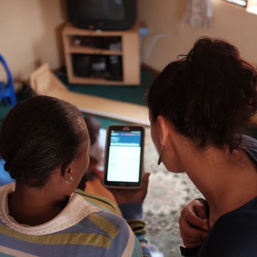 A photo looking over the shoulders of two women in Zambia who are using Count Me In on a tablet. The screen is illegible.