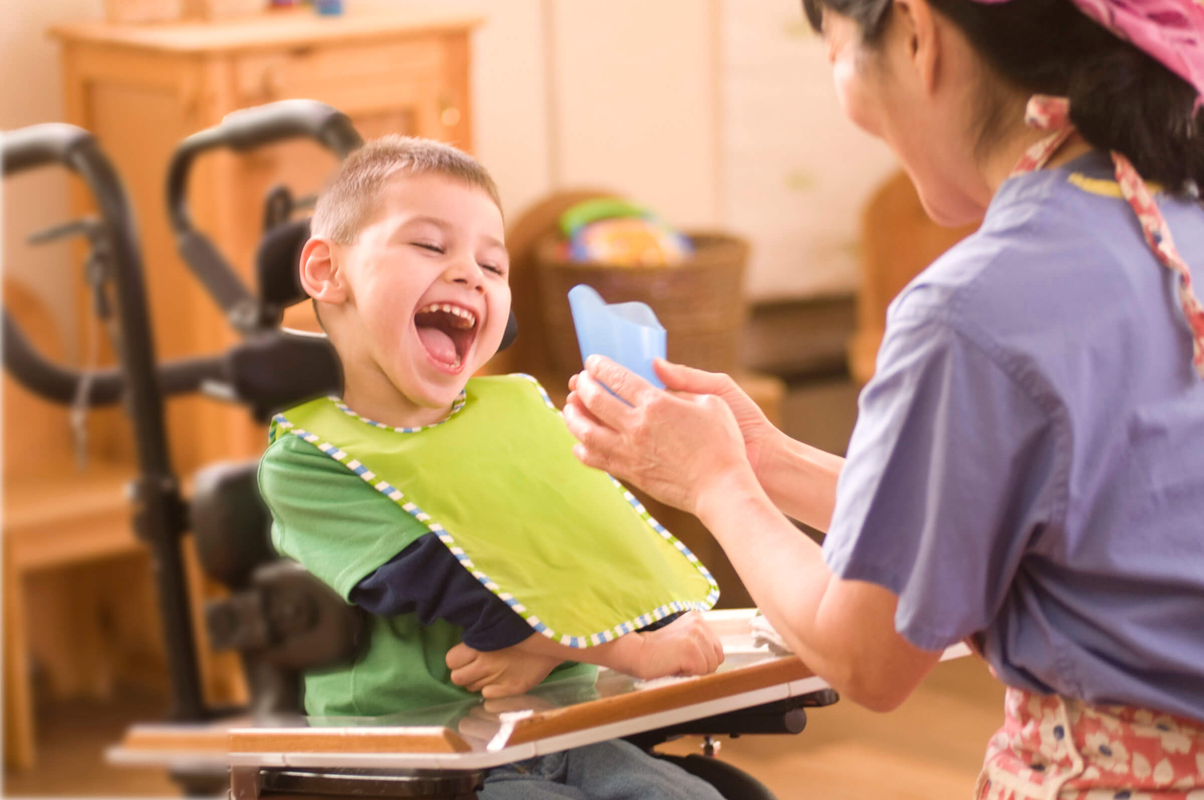 A photo of a young boy in a wheelchair smiling at a cut-out cup being presented by a woman.